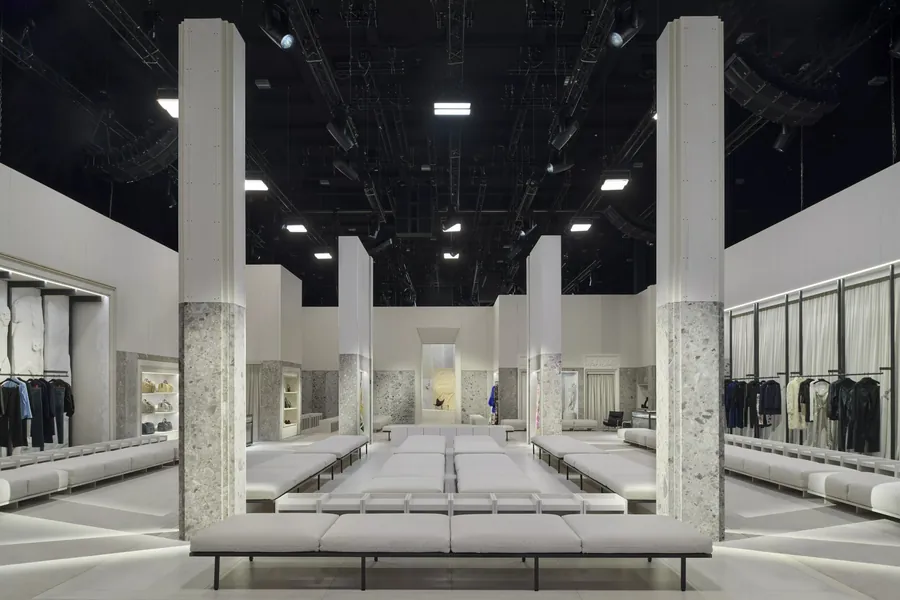 Gucci The Store Show: el espacio del desfile concebido como tienda, con bancos claros, columnas de piedra y percheros