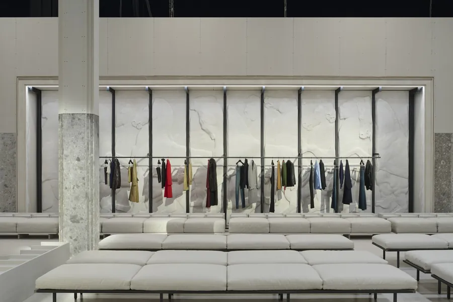 Gucci The Store Show: largo perchero ante una pared blanca en relieve, con bancos y una columna de piedra